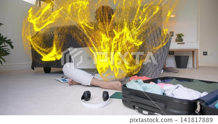 Sitting male typing on laptop on floor in bedroom, yellow particles rising, open suitcase Sitting male typing on laptop on floor in bedroom, yellow particles rising, open suitcase 141817889