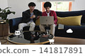 Sharing two men in jackets checking laptop on sofa at home with smartphone and digital icons 141817891