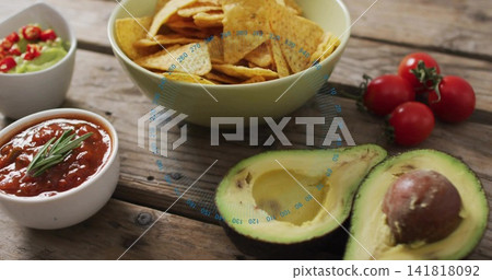 Displaying two halved avocados pit on rustic table pale-green chips-bowl, salsa, guac vine tomatoes Displaying two halved avocados pit on rustic table pale-green chips-bowl, salsa, guac vine tomatoes 141818092