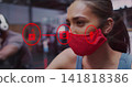 Pedaling woman wearing red cloth mask, blue tank top, on stationary bike at gym, overlay icons 141818386