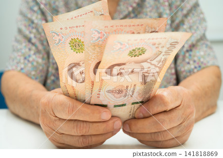 Asian elder senior woman patient holding Thai banknotes money in her hand, Cost of living and medical care. Asian elder senior woman patient holding Thai banknotes money in her hand, Cost of living and medical care. 141818869
