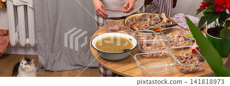 In a cozy home setting, a woman prepares kholodets, aspic, or jellied meat, traditional Ukraine dish, by packing cooked meat into glass dishes In a cozy home setting, a woman prepares kholodets, aspic, or jellied meat, traditional Ukraine dish, by packing cooked meat into glass dishes 141818973