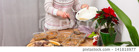 A woman stands by a table in a kitchen, preparing kholodets, aspic, or jellied meat, traditional Ukraine dish. A woman stands by a table in a kitchen, preparing kholodets, aspic, or jellied meat, traditional Ukraine dish. 141818977