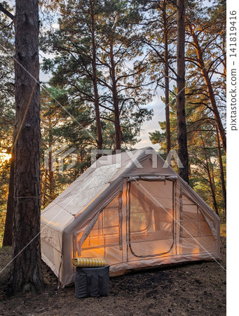 Glamping tent glowing at sunset among tall pine trees inside quiet forest campsite, warm interior light, soft sky behind branches, rustic outdoor retreat in nature Glamping tent glowing at sunset among tall pine trees inside quiet forest campsite, warm interior light, soft sky behind branches, rustic outdoor retreat in nature 141819416