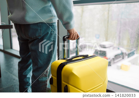 Man with yellow suitcase standing by window inside hotel Man with yellow suitcase standing by window inside hotel 141820033