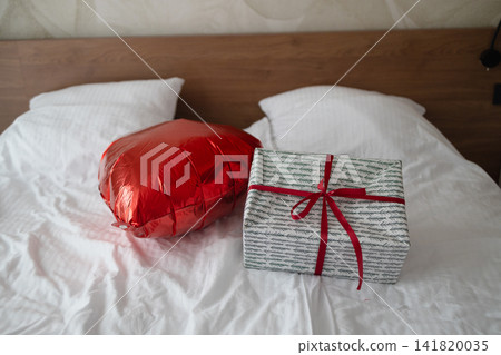 Red heart shaped balloon and gift box on bed Red heart shaped balloon and gift box on bed 141820035