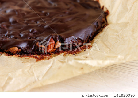 Closeup of freshly baked chocolate brownie with a glossy top and dense fudgy edge on parchment paper. Closeup of freshly baked chocolate brownie with a glossy top and dense fudgy edge on parchment paper. 141820080