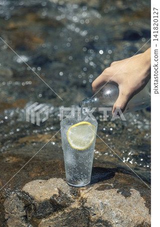 一隻手從清澈的夏日溪流中倒出檸檬味氣泡水。 一隻手從清澈的夏日溪流中倒出檸檬味氣泡水。 141820127