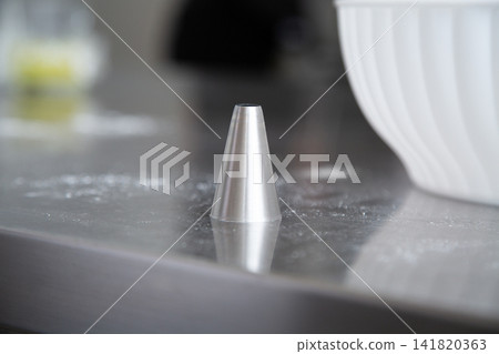 Stainless steel cone-shaped kitchen tool standing on reflective counter with soft blurred background and bright side light creating clean modern food preparation atmosphere Stainless steel cone-shaped kitchen tool standing on reflective counter with soft blurred background and bright side light creating clean modern food preparation atmosphere 141820363