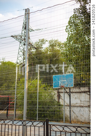Outdoor basketball court behind wire mesh fence with high voltage power transmission pylon Outdoor basketball court behind wire mesh fence with high voltage power transmission pylon 141820516