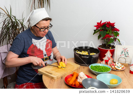 A woman cuts boiled potatoes while making Olivier salad, Russian salad, a traditional Ukrainian or Russian Christmas or New Year dish. The ingredients like carrots and peas are on the table A woman cuts boiled potatoes while making Olivier salad, Russian salad, a traditional Ukrainian or Russian Christmas or New Year dish. The ingredients like carrots and peas are on the table 141820639