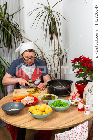 A woman is preparing Olivier salad, Russian salad, by chopping pickled cucumbers in her kitchen. She is surrounded by various ingredients on the table. It is a festive Christmas season in December A woman is preparing Olivier salad, Russian salad, by chopping pickled cucumbers in her kitchen. She is surrounded by various ingredients on the table. It is a festive Christmas season in December 141820647