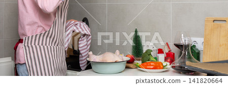 A man bakes chicken with potatoes in a kitchen while preparing for a pre-Christmas dinner. He focuses on his cooking tasks with fresh ingredients nearby, banner A man bakes chicken with potatoes in a kitchen while preparing for a pre-Christmas dinner. He focuses on his cooking tasks with fresh ingredients nearby, banner 141820664