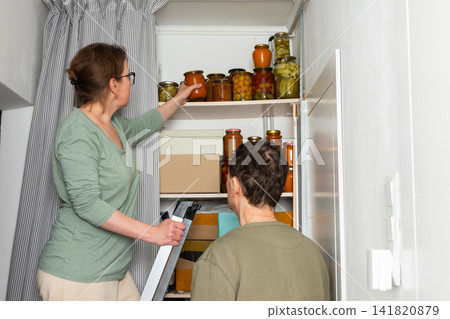 A married couple is busy placing canned goods on shelves in their pantry. They are in their city home, preparing for autumn. Boxes are organized, and the couple works together A married couple is busy placing canned goods on shelves in their pantry. They are in their city home, preparing for autumn. Boxes are organized, and the couple works together 141820879