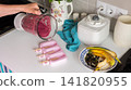 A woman is pouring a mixture of currant and banana homemade ice cream into pink molds in a kitchen. There are bananas and berries on the table nearby 141820955