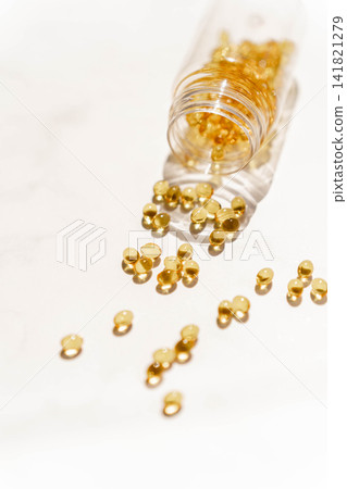 Golden softgel supplement capsules spilling from a transparent bottle Golden softgel supplement capsules spilling from a transparent bottle 141821279