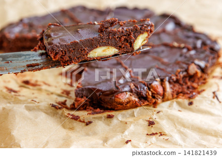 Closeup of a triangular slice of homemade chocolate almond brownie being lifted on a knife from the remaining cake. Selective focus 141821439