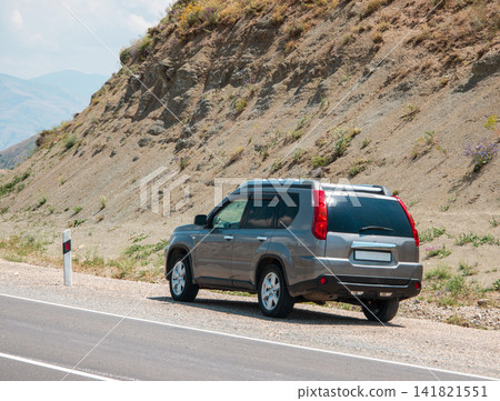 SUV pauses on winding road beside arid hill SUV pauses on winding road beside arid hill 141821551
