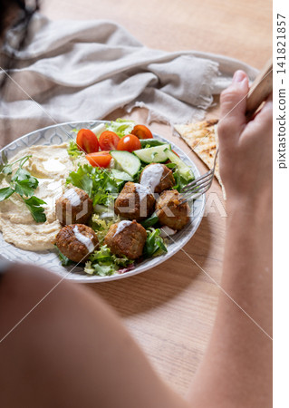Person holding plate of falafel with hummus and fresh salad Person holding plate of falafel with hummus and fresh salad 141821857