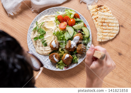 Person holding plate of falafel with hummus and fresh salad Person holding plate of falafel with hummus and fresh salad 141821858