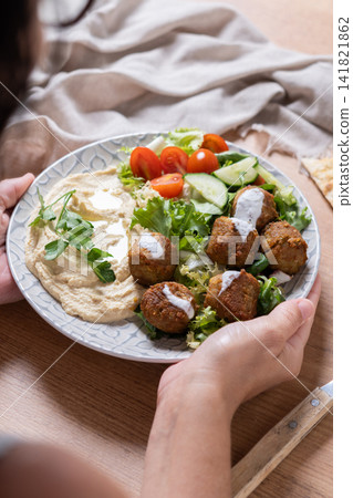 Person holding plate of falafel with hummus and fresh salad Person holding plate of falafel with hummus and fresh salad 141821862