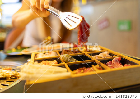 Person cooking korean barbecue raw meat with tongs Person cooking korean barbecue raw meat with tongs 141822379