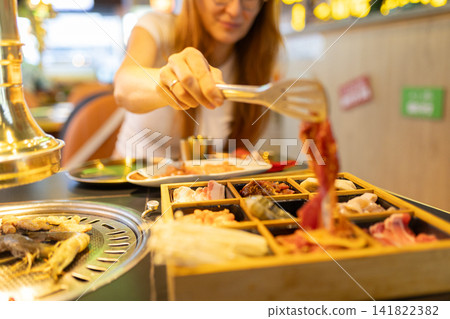 Woman grilling meat at korean barbecue restaurant 141822382