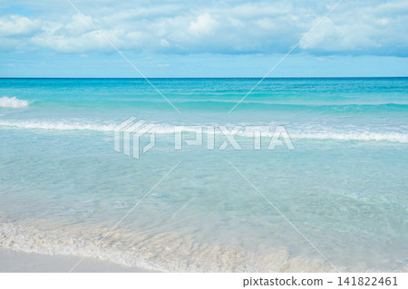 Calm ocean waves gently lap on the sandy shore under a bright blue sky Calm ocean waves gently lap on the sandy shore under a bright blue sky 141822461