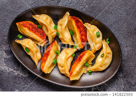Dumplings are served on a black plate with green onion Dumplings are served on a black plate with green onion 141822503