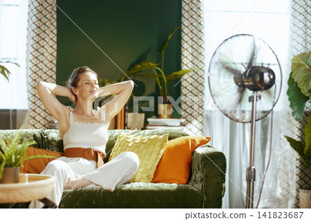 Woman Relaxing Comfortably with Fan in Living Room Woman Relaxing Comfortably with Fan in Living Room 141823687