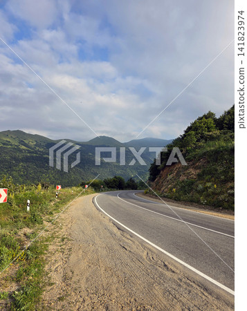 Winding asphalt road through green mountains under partly cloudy sky Winding asphalt road through green mountains under partly cloudy sky 141823974