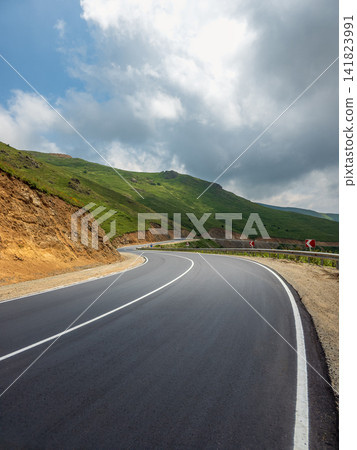 Scenic mountain road with white lines curves through forested terrain Scenic mountain road with white lines curves through forested terrain 141823991