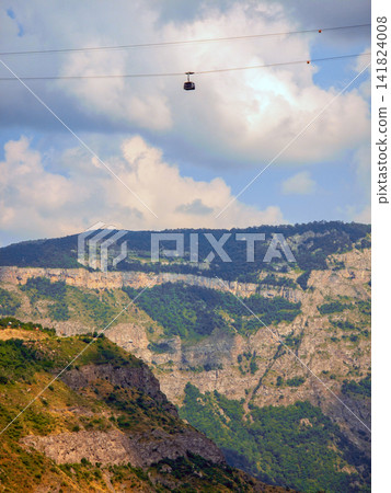 Cable car suspended between mountain peaks under partly cloudy skies 141824008