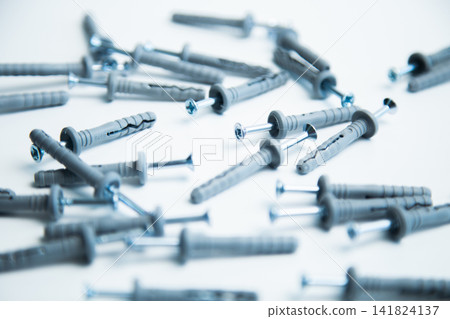 A lot of gray plastic dowels with screwed screws are chaotically scattered on a white background with a blurring effect. The concept of mass fasteners, home repairs, installation works. High quality A lot of gray plastic dowels with screwed screws are chaotically scattered on a white background with a blurring effect. The concept of mass fasteners, home repairs, installation works. High quality 141824137