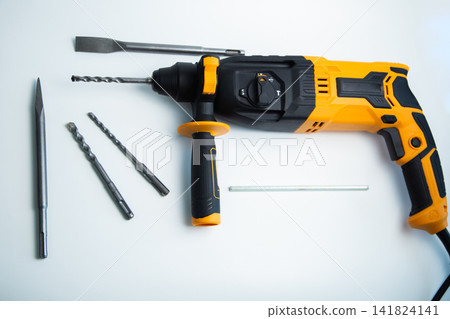 Top view of a yellow and black perforator with a handle, a set of drills, chisels and fasteners on a white background. The concept of a complete set for construction work, universal power tools. High 141824141