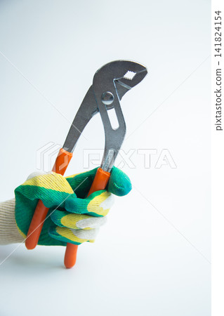 A gloved hand confidently holds a metal adjustable wrench with bright orange handles vertically on a clean white background. The concept of plumbing works, reliable hand tools. High quality photo 141824154