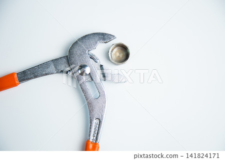 Close-up view of the adjustable large wrench from above is open and between its teeth lies a pipe plug lying on a white background in the center. The concept of repair, plumbing, settings. High Close-up view of the adjustable large wrench from above is open and between its teeth lies a pipe plug lying on a white background in the center. The concept of repair, plumbing, settings. High 141824171