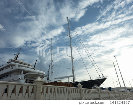 Luxury motor and sailing yachts moored in a marina behind a stone wall with clouds in the sky Luxury motor and sailing yachts moored in a marina behind a stone wall with clouds in the sky 141824337