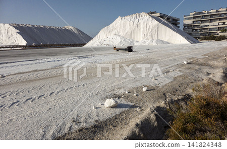 Massive white sea salt mounds are gathered at an industrial salt evaporation plant near homes under a clear sky Massive white sea salt mounds are gathered at an industrial salt evaporation plant near homes under a clear sky 141824348