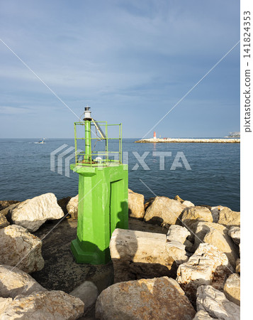 Bright green navigation light beacon on rocky harbor pier with calm blue sea and sky Bright green navigation light beacon on rocky harbor pier with calm blue sea and sky 141824353