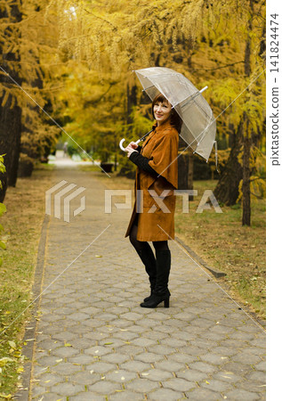 Woman in a brown coat stands amidst autumn leaves in a serene park setting on a clear day Woman in a brown coat stands amidst autumn leaves in a serene park setting on a clear day 141824474