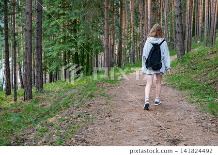 Young woman walking along a forest path surrounded by tall trees. Young woman walking along a forest path surrounded by tall trees. 141824492