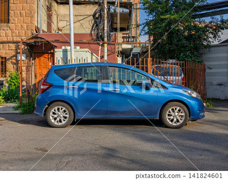 Side view of blue compact car parked outdoors near fences and buildings Side view of blue compact car parked outdoors near fences and buildings 141824601