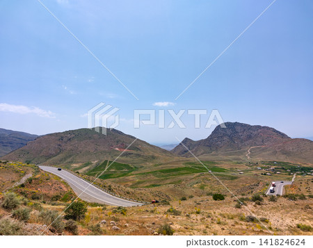 Highway curves across rocky hillsides with distant mountain peaks Highway curves across rocky hillsides with distant mountain peaks 141824624