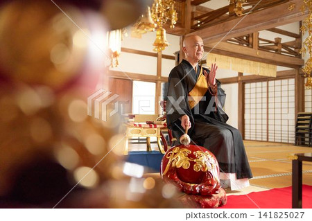 一位男僧人坐在寺廟的大殿裡，敲擊著木製魚鼓。 141825027