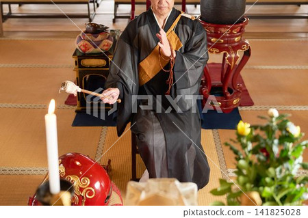 A male monk sits in the main hall of a temple and strikes a wooden fish drum. A male monk sits in the main hall of a temple and strikes a wooden fish drum. 141825028
