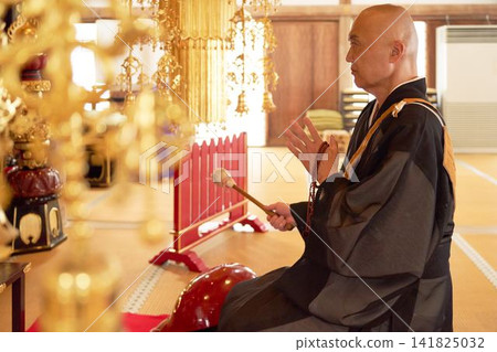 一位僧人坐在寺廟大殿裡，側身敲擊木製魚鼓。 141825032