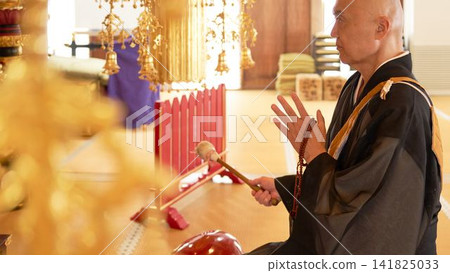 一位僧人坐在寺廟大殿裡，側身敲擊木製魚鼓。 141825033
