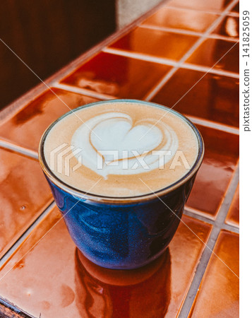 Blue cup of cappuccino with heart shaped latte art on orange tiled table Blue cup of cappuccino with heart shaped latte art on orange tiled table 141825059