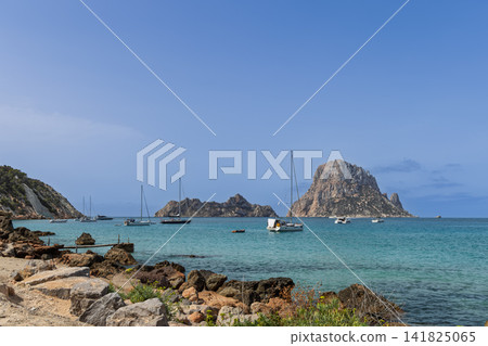 Es Vedra and Es Vedranell off Cala d Hort with anchored sailboats and rocky shoreline. Es Vedra and Es Vedranell off Cala d Hort with anchored sailboats and rocky shoreline. 141825065